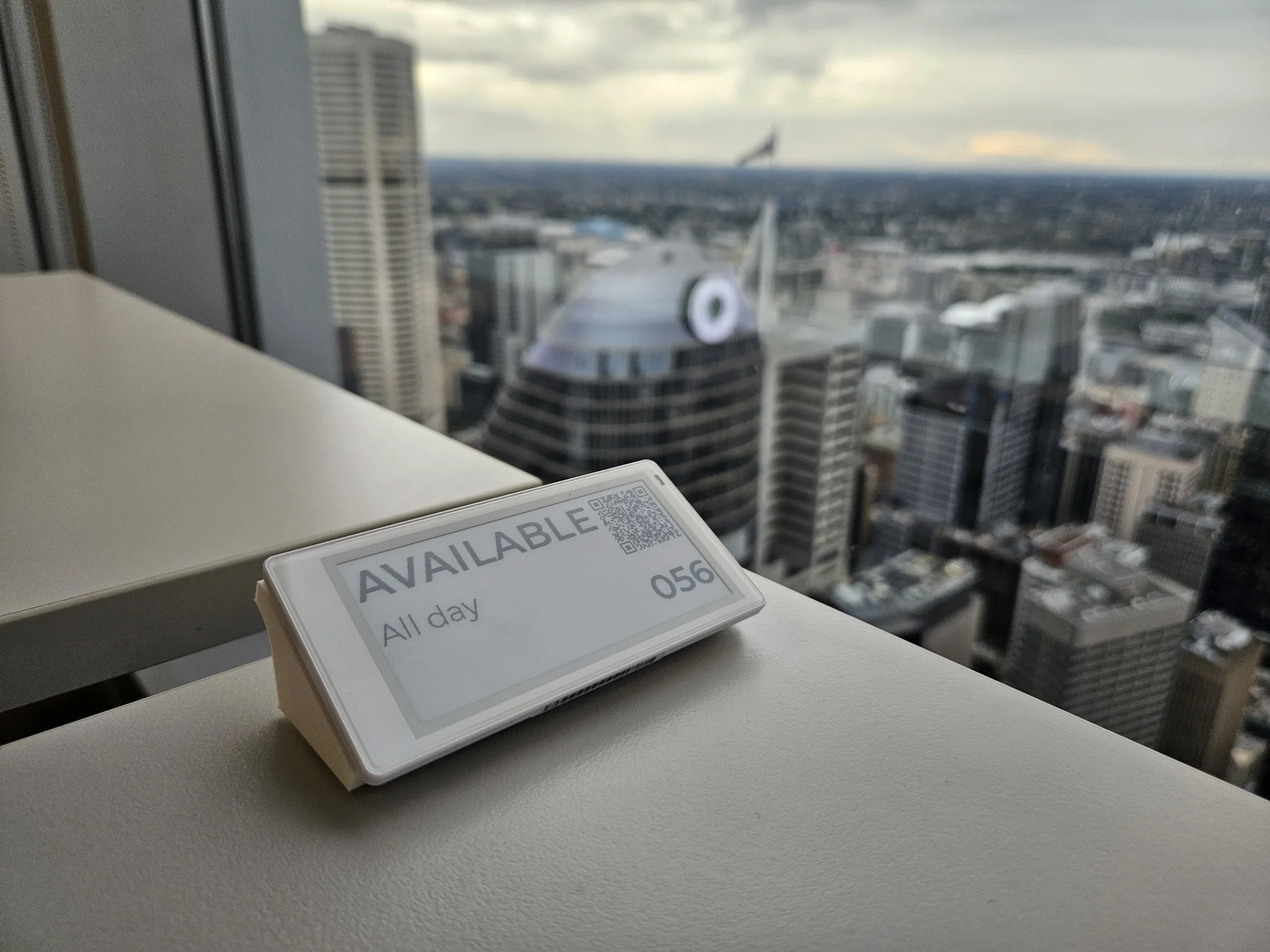 Smart Desk Label for desk 056 on an angled stand beside an office window overlooking the city